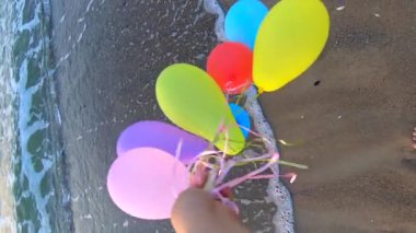 Deniz dalgalarının yakınındaki kumlu sahil sahillerinde renkli balonlarla oynayan kişi. Çok renkli küçük balonlar elinde kurdeleyle kumun üzerine bağlanmıştı. Dinlenme eğlencesi şımartma eğlence eğlencesi