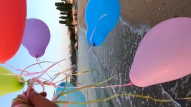 Deniz dalgalarının yakınındaki kumlu sahil sahillerinde renkli balonlarla oynayan kişi. Çok renkli küçük balonlar elinde kurdeleyle kumun üzerine bağlanmıştı. Dinlenme eğlencesi şımartma eğlence eğlencesi