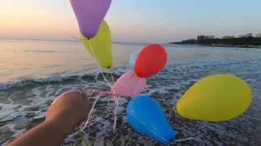 Deniz dalgalarının yakınındaki kumlu sahil sahillerinde renkli balonlarla oynayan kişi. Çok renkli küçük balonlar elinde kurdeleyle kumun üzerine bağlanmıştı. Dinlenme eğlencesi şımartma eğlence eğlencesi