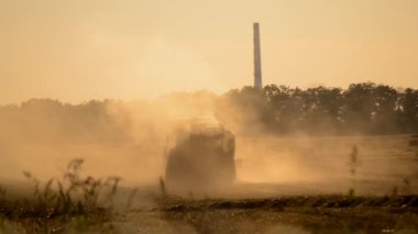 Güneşli bir yaz akşamında hasat makinası samanı balya sürüş sahasına sıkıştırıyor. Buğday balyalarıyla dolu bir tarla. Sahada çok toz var. Tarım endüstrisi tarımsal hasat çalışmaları