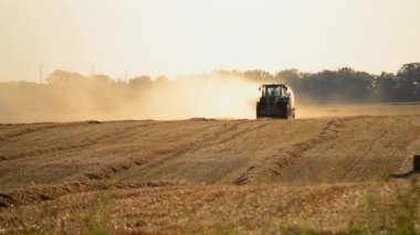 Güneşli bir yaz akşamında hasat makinası samanı balya sürüş sahasına sıkıştırıyor. Buğday balyalarıyla dolu bir tarla. Sahada çok toz var. Tarım endüstrisi tarımsal hasat çalışmaları