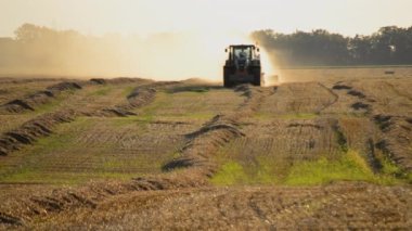 Güneşli bir yaz akşamında hasat makinası samanı balya sürüş sahasına sıkıştırıyor. Buğday balyalarıyla dolu bir tarla. Sahada çok toz var. Tarım endüstrisi tarımsal hasat çalışmaları