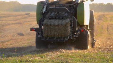 Güneşli bir yaz akşamında hasat makinası samanı balya sürüş sahasına sıkıştırıyor. Buğday balyalarıyla dolu bir tarla. Sahada çok toz var. Tarım endüstrisi tarımsal hasat çalışmaları