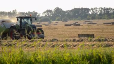 Bila Tserkva, Ukrayna, 19 Ağustos 2023: Tarladan samana saman döşeyen hasat makinesini sürüş sahasına birleştirin. Güneşli bir yaz akşamı. Buğday balyalarıyla dolu bir tarla. Sahada çok toz var. Tarım