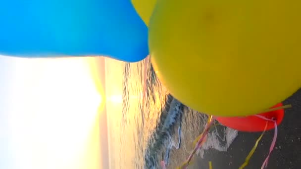 日出和日落时 手和许多色彩艳丽的气球系在沙滩上的带子上 多色气球在黎明时分 慢动作海滨 阳光透过球体闪耀 — 图库视频影像