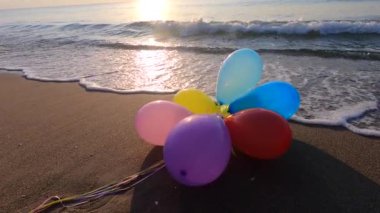 Deniz kıyısındaki kumlu kumsalda, gün batımında ve şafakta deniz dalgaları üzerinde bir grup çok renkli balon. Sanat yaratıcılığı