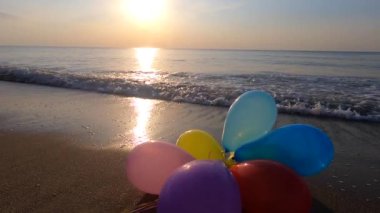 Deniz kıyısındaki kumlu kumsalda, gün batımında ve şafakta deniz dalgaları üzerinde bir grup çok renkli balon. Sanat yaratıcılığı