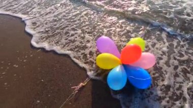Deniz kıyısındaki kumlu kumsalda, gün batımında ve şafakta deniz dalgaları üzerinde bir grup çok renkli balon. Sanat yaratıcılığı