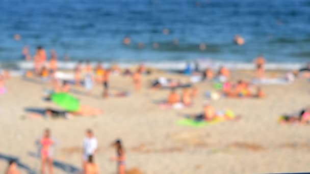 许多人在海滨沙滩上休息 在阳光灿烂的炎炎夏日在海里游泳 许多白种人在公共海滩上生活 休假日放松活动 模糊的背景 — 图库视频影像