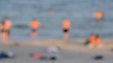 Birçok insan sıcak bir yaz gününde kumlu sahil sahillerinde dinleniyor ve denizde yüzüyor. Yazın halk plajında bir sürü beyaz tenli insan. Tatilde dinlenme aktivitesi. Bulanık arkaplan