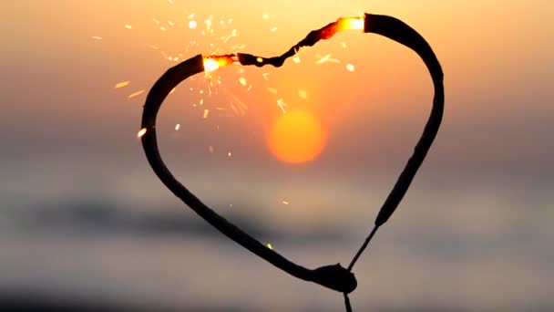 海の背景に燃えるハート型のスパークラー 夜明けに太陽が昇る ベンガル火災は 日の出の夜明けと海の日没に輝く心の形で インフレーション バレンタインデー — ストック動画