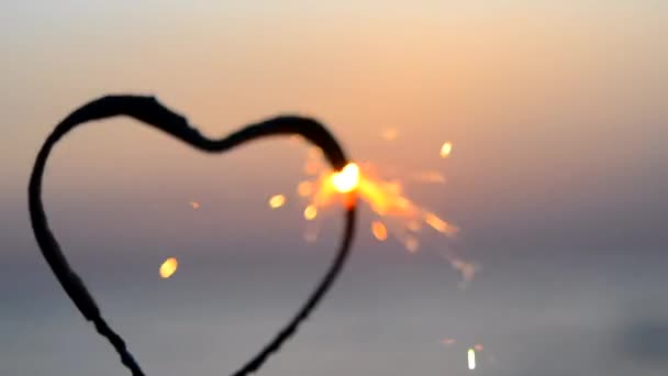 夜明けに海の背景に燃えているハート型のスパークラー ベンガル火災は 日の出の夜明けと海の日没に輝く心の形で インフレーション バレンタインデー — ストック動画