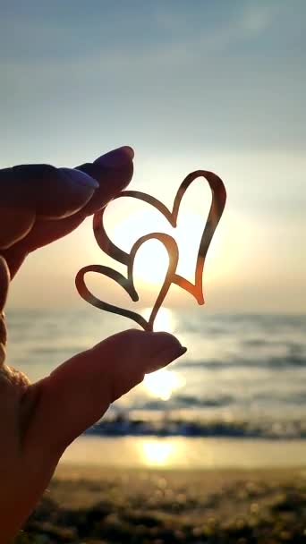 海の夜明けの日没に太陽の背景に対して2つのハートの形をした指の黒い輪郭を保持する女性 コンセプト愛 ロマンチックなバレンタインデー — ストック動画