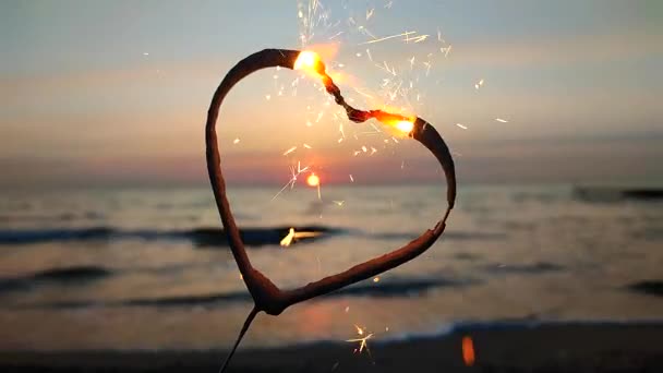 ハートの形をしたスパークラーは 海の背景に燃え 夜明けに太陽が昇る ベンガル火災は 日の出の夜明けと海の日没に輝く心の形で コンセプト インフォメーション バレンタインデー — ストック動画