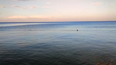Akşam denizi sakin görünüyor. Pembe turuncu gökyüzü ve akşam vakti beyaz bulutlar. Deniz suyunun pürüzsüz mavi yüzeyi. Suda kısıtlı şamandıralar var. Sakin bir hava. Soyut doğal arkaplan