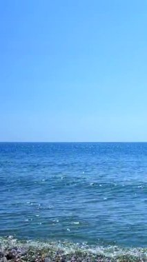 Küçük mavi deniz dalgaları, mavi bulutsuz gökyüzü ve güneşli bir yaz gününde ufuk çizgisi. Sudaki dalgalar ve su yüzeyindeki beyaz güneş. Sakin deniz. Rüzgârsız sakin hava. Dikey