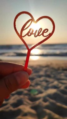 Parmaklarını tutan kişi kırmızı kalbe ve sözcüğe sarılır. Arka planda aşk, deniz ve deniz dalgaları, güneşli yaz günlerinde mavi gökyüzü. Aziz Sevgililer Günü Düşey Aşkı kavramını kabul et