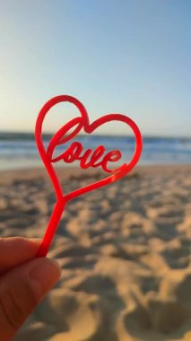 El ele tutuşan kişi el ele tutuşur kırmızı kalp ve aşk arka planda deniz ve deniz dalgaları, güneşli yaz günlerinde mavi gökyüzü. Aşk romantizmi kavramı Aziz Sevgililer Günü Dikey