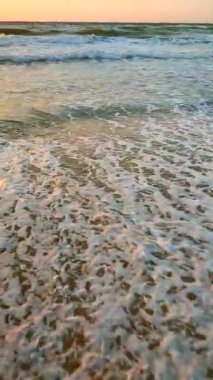 Fırtınalı deniz. Gün batımında ve şafakta denizde beyaz köpüklü büyük dalgalar. Mavi deniz, turuncu kırmızı gökyüzü, güneş. Sahil kıyısı kıyı şeridi. Doğal arka plan fırtınası Yavaş çekim düşey