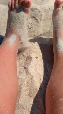 Ayaklarını kuma gömmüş bir kadın. Sıcak yaz gününde kumsalda ayaklarını kuru kuma gömme oyunu oynayan biri. Tatil tatili, dinlenme, dinlenme turizmi, ufalanan dikey