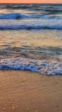 Fırtınalı deniz. Gün batımında ve şafakta denizde beyaz köpüklü büyük dalgalar. Mavi deniz, turuncu kırmızı gökyüzü, güneş. Sahil kıyısı kıyı şeridi. Doğal arka plan fırtınası Yavaş çekim düşey