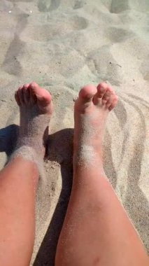 Ayaklarını kuma gömmüş bir kadın. Sıcak yaz gününde kumsalda ayaklarını kuru kuma gömme oyunu oynayan biri. Tatil tatili, dinlenme, dinlenme turizmi, ufalanan dikey