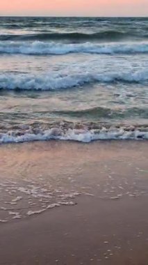 Fırtınalı deniz. Gün batımında ve şafakta denizde beyaz köpüklü büyük dalgalar. Mavi deniz, turuncu kırmızı gökyüzü. Sahil kıyısı kıyı şeridi. Doğal arkaplan doğa fırtına düşey