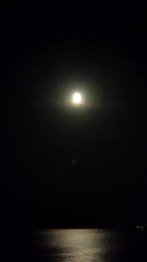 Gökyüzündeki ay ve gece deniz kıyısındaki deniz dalgaları üzerinde ay ışığı yolu. Su yüzeyindeki ay yolu. Deniz dalgaları üzerinde ay ışığından parlıyor. Doğal arkaplan Doğa dikey arkaplan