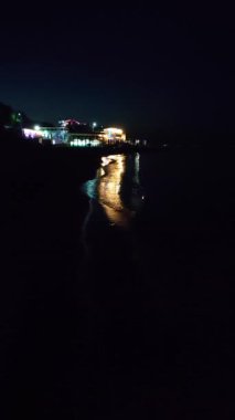 Deniz kıyısındaki binaların parlayan ışıklarının yansıması. Gece deniz dalgalarının sularında. Deniz kıyısında ışıklı lambaları olan binalar. Gece deniz kıyısındaki şehir. Suda aydınlanma. Dikey