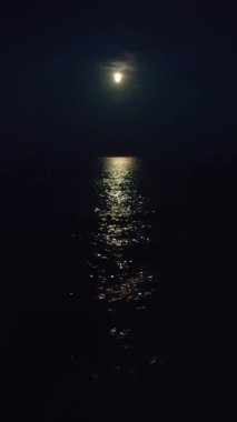 Gökyüzündeki ay ve gece deniz kıyısındaki deniz dalgaları üzerinde ay ışığı yolu. Su yüzeyindeki ay yolu. Deniz dalgaları üzerinde ay ışığından parlıyor. Doğal arkaplan Doğa dikey arkaplan