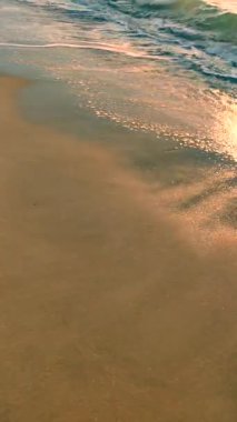 Mavi deniz, kumlu sahil ve güneşli yaz gününde deniz dalgalarının yüzeyinde parlayan güneş. Güneşli bir günde kumlu sahil sahillerinde dalgalar halinde akan mavi deniz. Beyaz köpük, deniz kuzuları. Doğal arka plan. Dikey