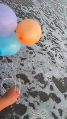 Güçlü rüzgarlarda denizin arka planında üç renkli şişme top. Elinde çok renkli hava balonlarıyla kumlu sahil kıyılarında arka planda deniz dalgalarıyla oynayan biri. Eğlence eğlencesi Dikey