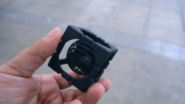 Elinde üç boyutlu bir yazıcıya basılmış bir nesne tutan bir kişi. Erimiş plastikten yapılmış 3 boyutlu bir yazıcıya basılmış geometrik model. Siyah şekil 3D yazıcı tarafından oluşturuldu. FDM teknolojisi.