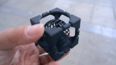Elinde üç boyutlu bir yazıcıya basılmış bir nesne tutan bir kişi. Erimiş plastikten yapılmış 3 boyutlu bir yazıcıya basılmış geometrik model. Siyah şekil 3D yazıcı tarafından oluşturuldu. FDM teknolojisi.
