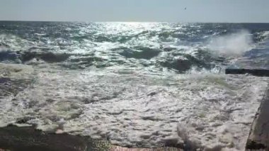 Fırtına. Denizde fırtına. Beyaz köpüklü büyük açık deniz dalgaları beton iskele duvarına çarpıyor ve güneşli bir yaz gününde su sıçrıyor. Fırtınalı deniz havası. Dalgalı deniz. Kıyıya ve dalgalara. Doğa. Doğal arkaplan