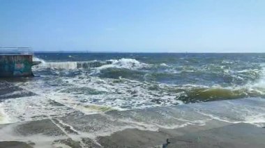 Fırtına. Denizde fırtına. Beyaz köpüklü büyük açık deniz dalgaları beton iskele duvarına çarpıyor ve güneşli bir yaz gününde su sıçrıyor. Fırtınalı deniz havası. Dalgalı deniz. Kıyıya ve dalgalara. Doğa. Doğal arkaplan
