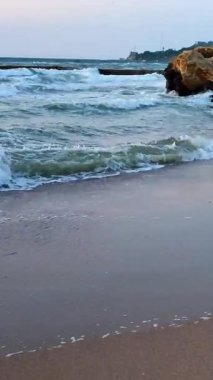 Fırtınalı deniz. Gün batımında ve şafakta denizde beyaz köpüklü büyük dalgalar. Mavi deniz, turuncu kırmızı gökyüzü. Sahil kıyısı kıyı şeridi. Doğal arkaplan doğa fırtına düşey