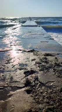 Güneşli bir yaz gününde, fırtınada, eski bir dalgakıran iskelesinin kenarında duran insanlar. Deniz kıyısındaki sahil şeridinde dalgakıran. Fırtına sırasında büyük dalgalarla denize ıslak iskele