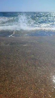 Güneşli bir yaz gününde büyük dalgalar eski bir çimento iskelesine çarpıyor. Beyaz köpüklü deniz dalgaları, mavi deniz, mavi gökyüzü, kahverengi toprak seti. Yavaş çekim