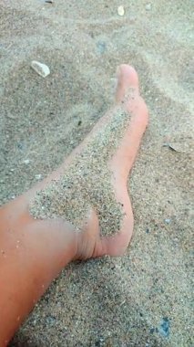 Dişi ayağına kumlu bir plaja kum serpilmiş. Kumlu bir sahilde kumla kaplı bir kadın bacağı