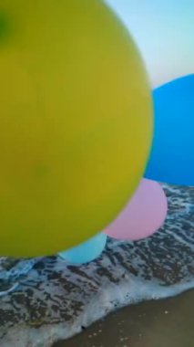 Sabahın erken saatlerinde deniz kıyısında renkli balonlarla oynayan biri. Gün batımında deniz kenarında çok renkli hava balonlarıyla oynayan kişi. Kumlu sahil kıyısında hava balonları. Dikey