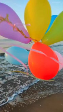 Sabahın erken saatlerinde deniz kıyısında renkli balonlarla oynayan biri. Gün batımında deniz kenarında çok renkli hava balonlarıyla oynayan kişi. Kumlu sahil kıyısında hava balonları. Dikey