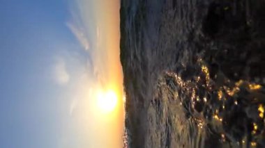 Deniz ve güneş. Dalgalanan dalgalar ve güneşli yollarla deniz suyu yüzeyi. Şafakta ve gün batımında parlayan güneş. Mavi gökyüzü ve beyaz tüy bulutları. Açık gökyüzü denizi. Alt açı. Yuvarlanan dalga. Su altı Görünümü Dikey