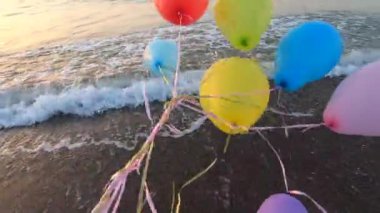 Deniz dalgalarının yakınındaki kumlu sahil sahillerinde renkli balonlarla oynayan kişi. Çok renkli küçük balonlar elinde kurdeleyle kumun üzerine bağlanmıştı. Dinlenme eğlencesi şımartma eğlence eğlencesi