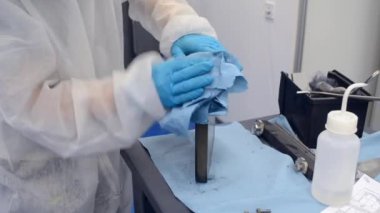 Beyaz Koruyucu Takım Elbise ve Mavi Koruyucu Eldiven Giyen İşçi Endüstriyel Ekipman için Metal Parçalarını Temizliyor. Dezenfektan Sıvı Sıvı Sıvı ve Peçeteyi Yüzey Metalinin Üzerine Döküyor