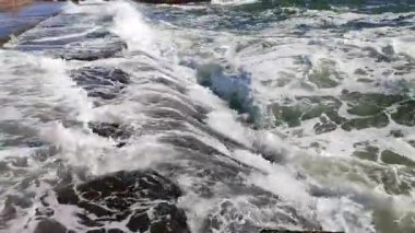 Beyaz köpüklü büyük deniz dalgaları, güneşli bir yaz gününde şehirde fırtına sırasında insanların üzerinde durduğu beton iskeleye çarpıp sıçrıyor. Fırtınalı deniz. Deniz manzarası, fırtına sırasında açık deniz dalgaları..