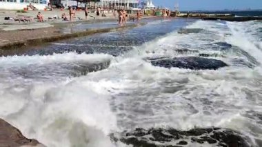 Odessa, Ukrayna, 30 Ağustos 2023: Güneşli bir yaz gününde şehrin fırtınası sırasında üzerinde insanların durduğu beyaz köpüklü büyük deniz dalgaları beton iskeleye çarpıp sıçrıyor. Fırtınalı deniz.
