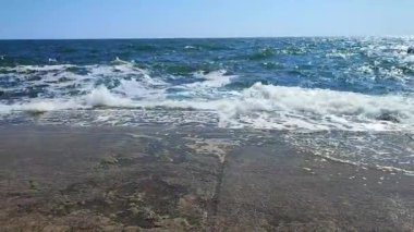 Güneşli bir yaz gününde büyük dalgalar eski bir çimento iskelesine çarpıyor. Beyaz köpüklü deniz dalgaları, mavi deniz, mavi gökyüzü, kahverengi set..