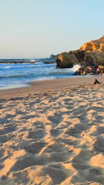 Kumlu sahil kıyısı, mavi su ve güneşli bir yaz sabahında sarı kayalar. Dikey