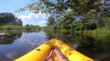 Güneşli bir yaz gününde yeşil çimen kamışları arasında sakin bir nehrin yüzeyinde şişme bir teknede yüzen bir insan. Bakış açısı. Sakin nehirde kano yapıyorum. Turizm, eğlence, eğlence.